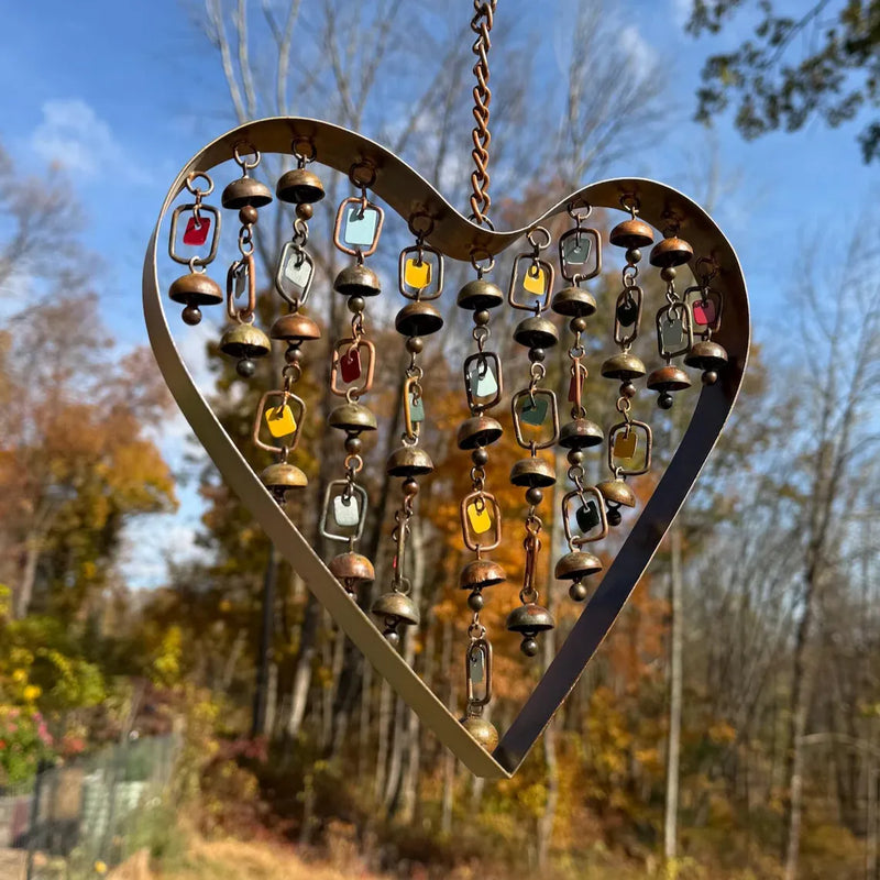 Heart-shaped metal wind chime with colorful accents and small bells against a clear blue sky