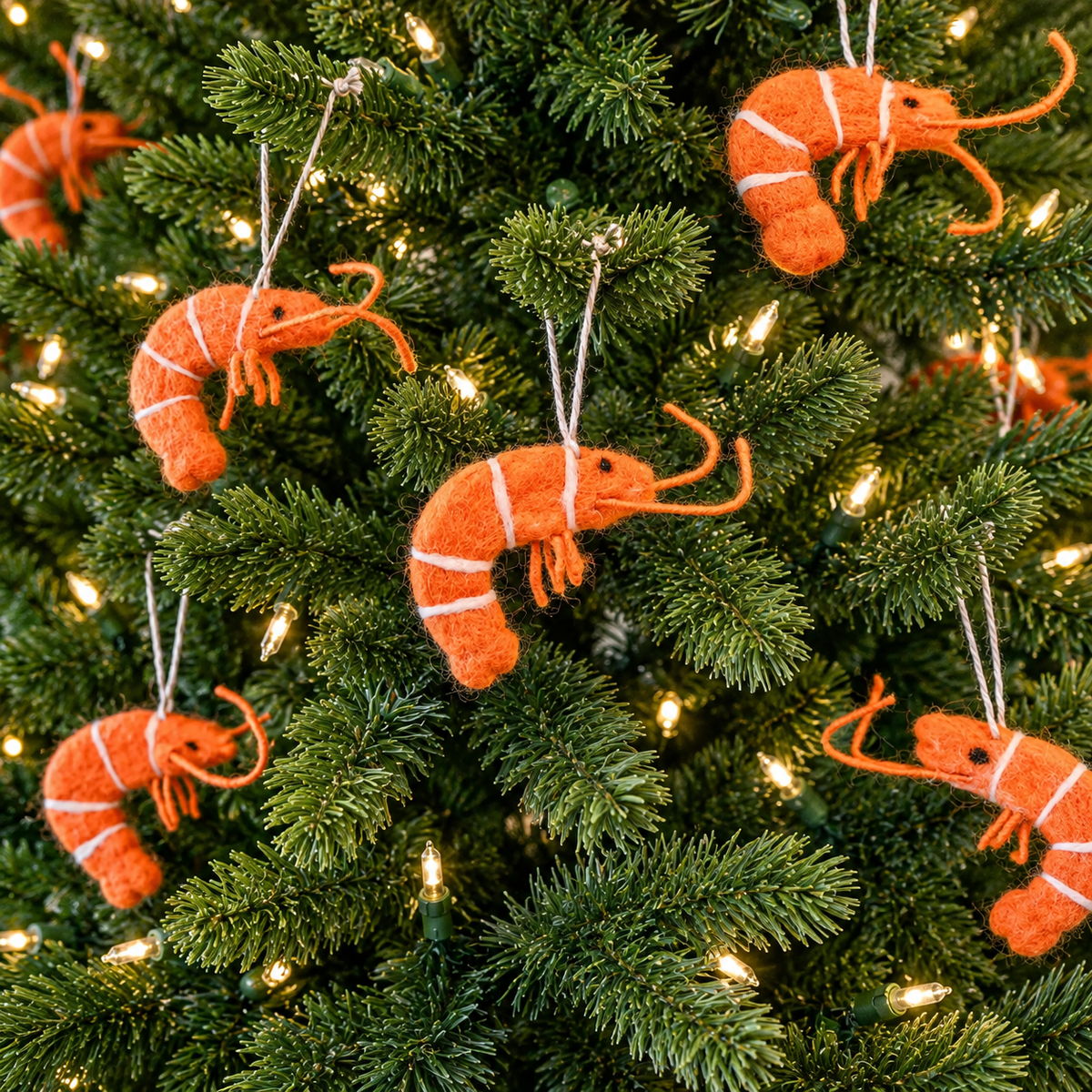 Several orange prawn felt ornaments hanging among illuminated Christmas tree branches