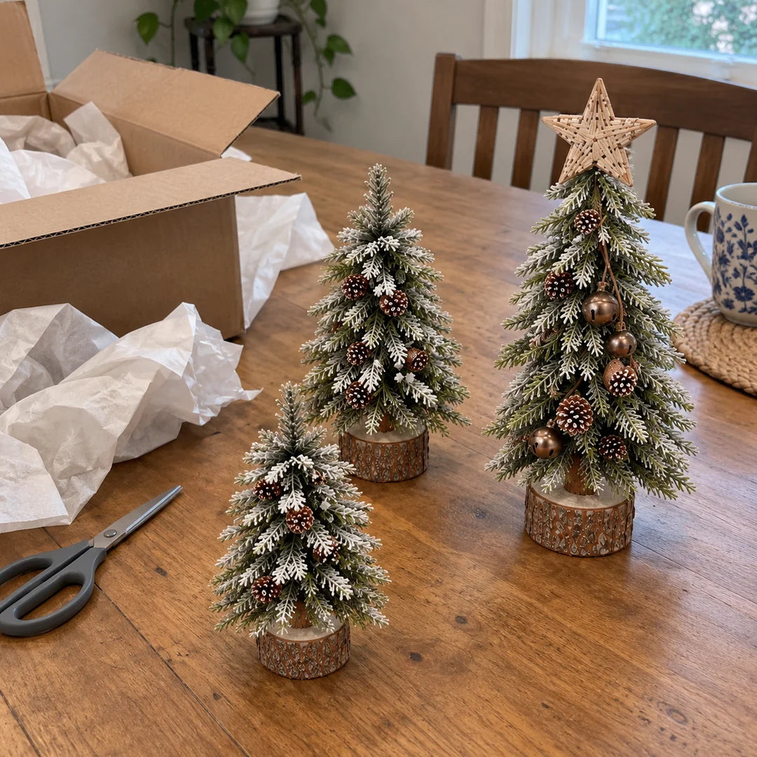 Three snowy mini Christmas trees unpacked on a wooden dining table
